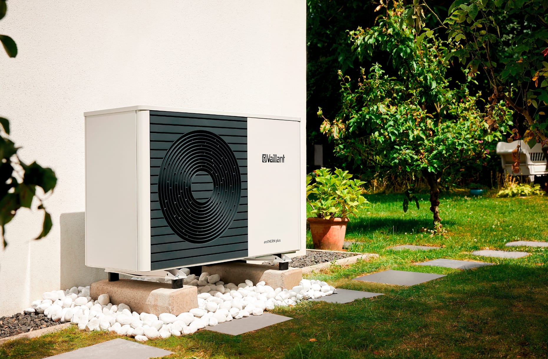 Vaillant warmtepomp geplaatst naast een muur met een tuin op de achtergrond.